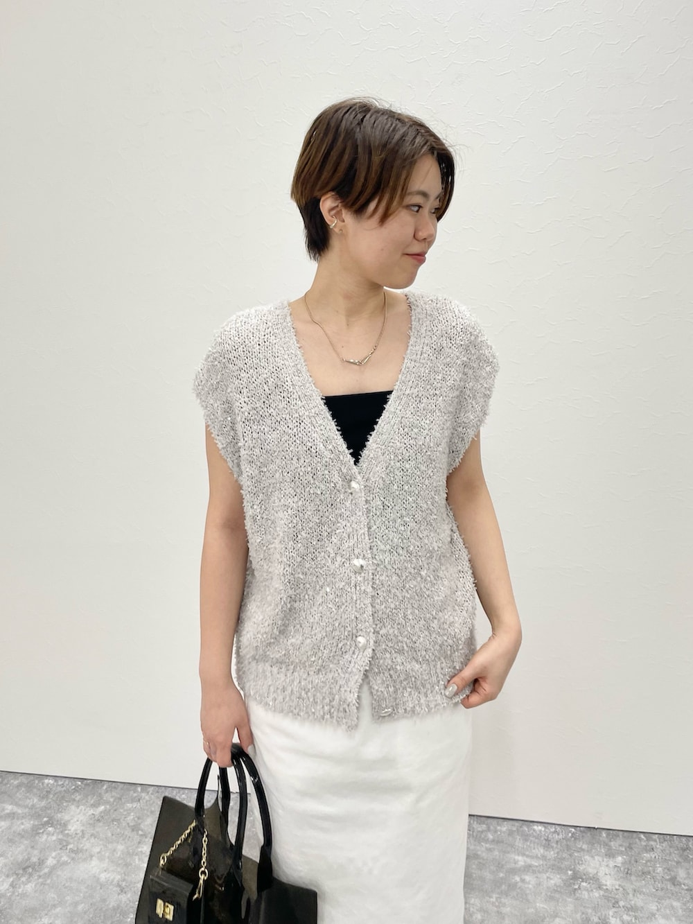 ベージュ系のベスト、ホワイト系のスカート、ブラック系のトートバッグを着用したレディースの春コーディネートの2枚目の写真