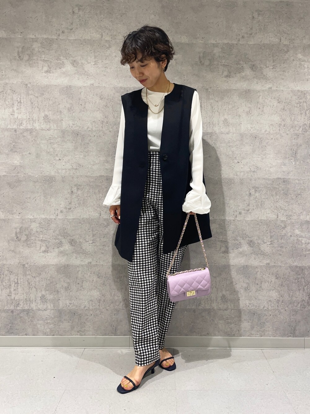 ブラック系のベスト、ホワイト系のニット/セーター、パープル系のショルダーバッグを着用したレディースの春コーディネートの6枚目の写真