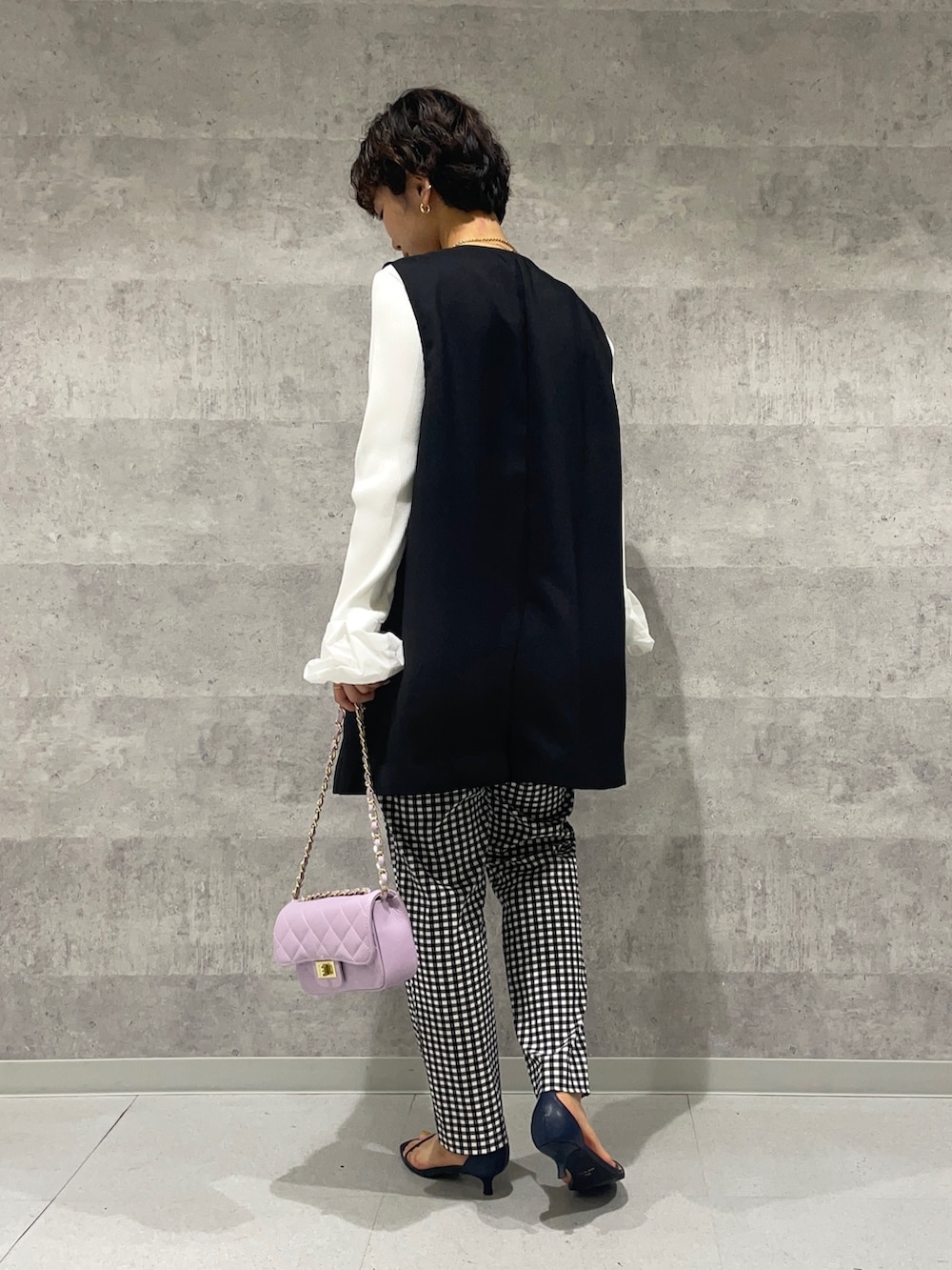 ブラック系のベスト、ホワイト系のニット/セーター、パープル系のショルダーバッグを着用したレディースの春コーディネートの4枚目の写真