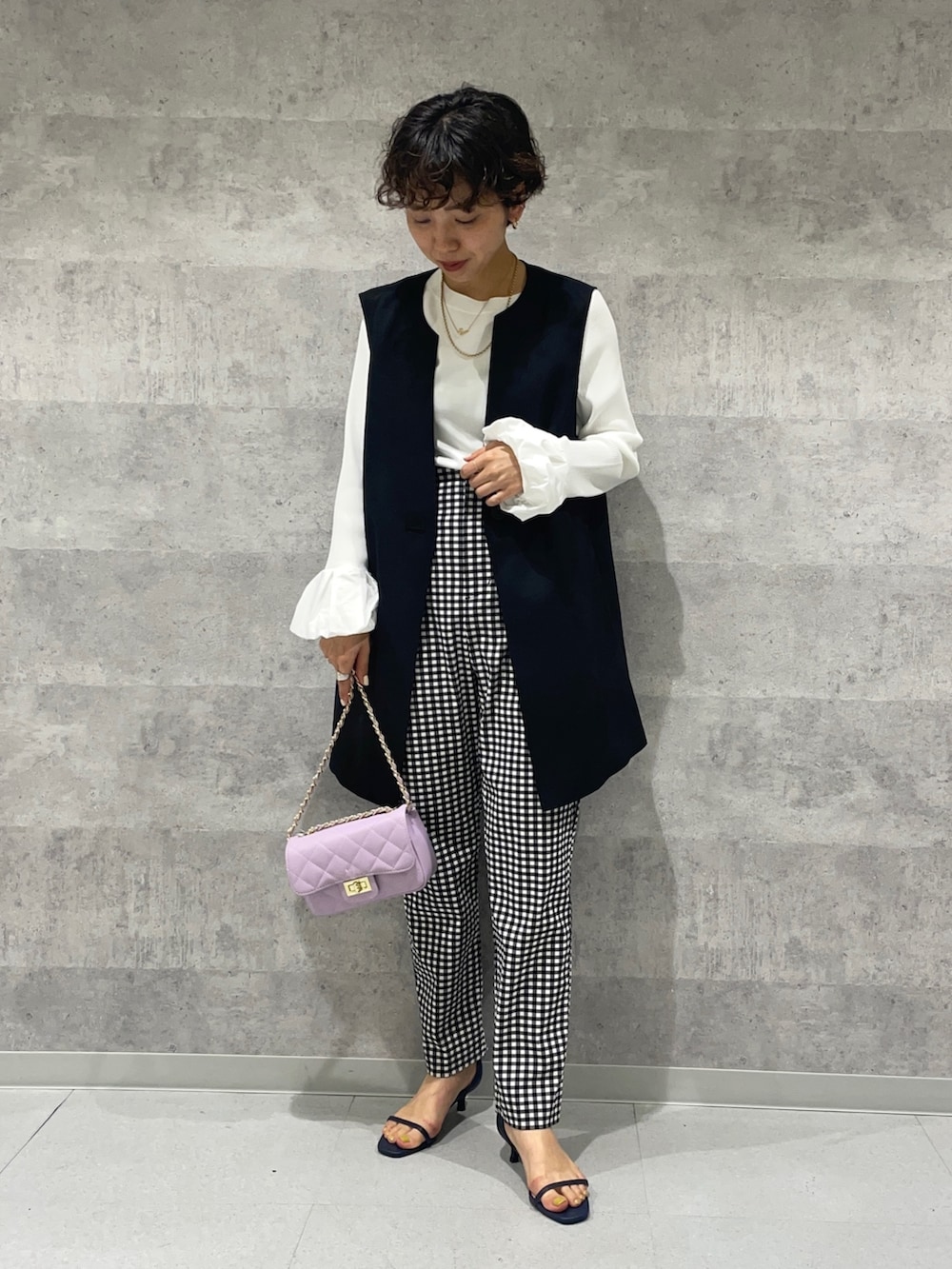 ブラック系のベスト、ホワイト系のニット/セーター、パープル系のショルダーバッグを着用したレディースの春コーディネートの2枚目の写真