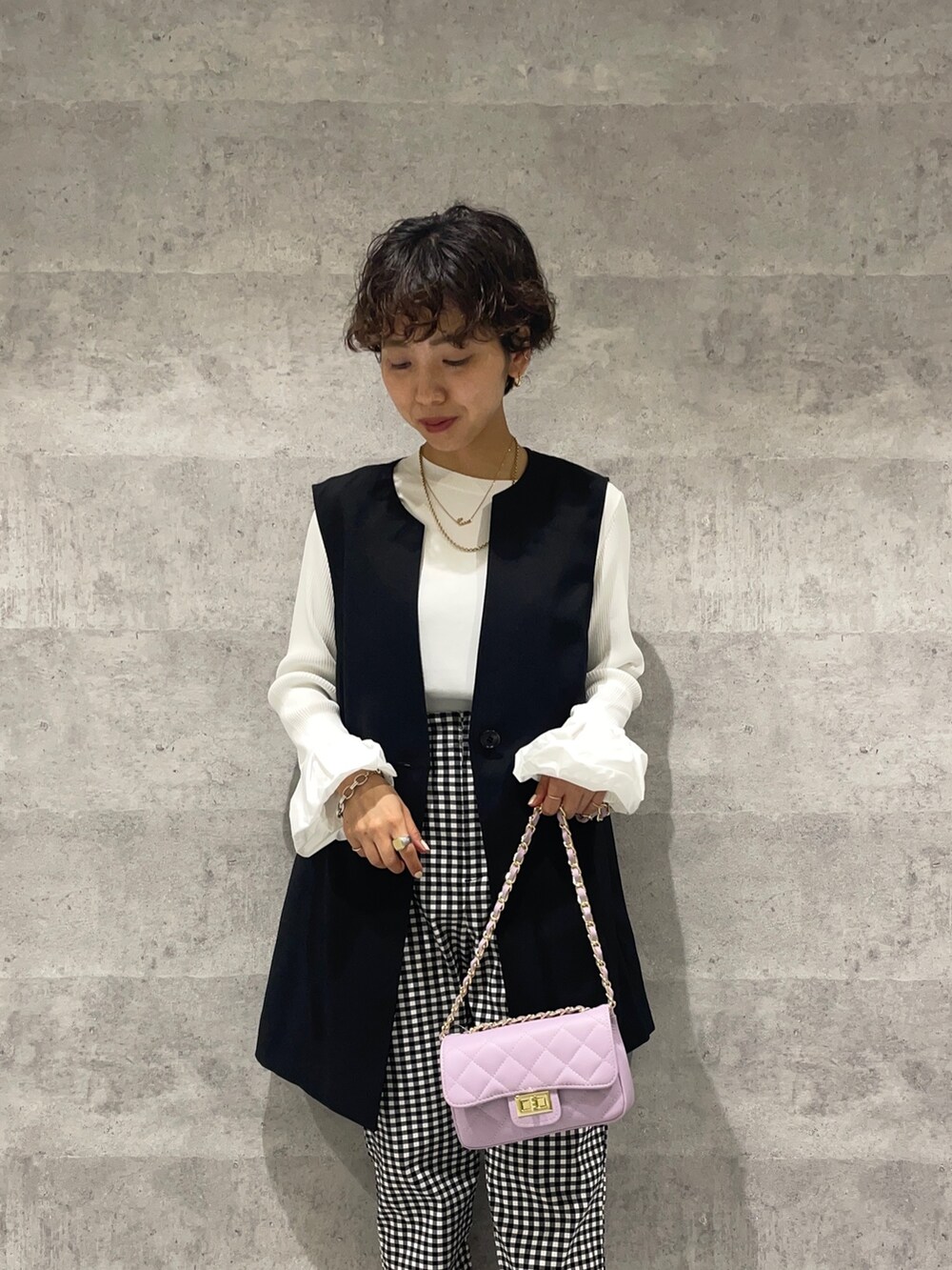 ブラック系のベスト、ホワイト系のニット/セーター、パープル系のショルダーバッグを着用したレディースの春コーディネートの5枚目の写真