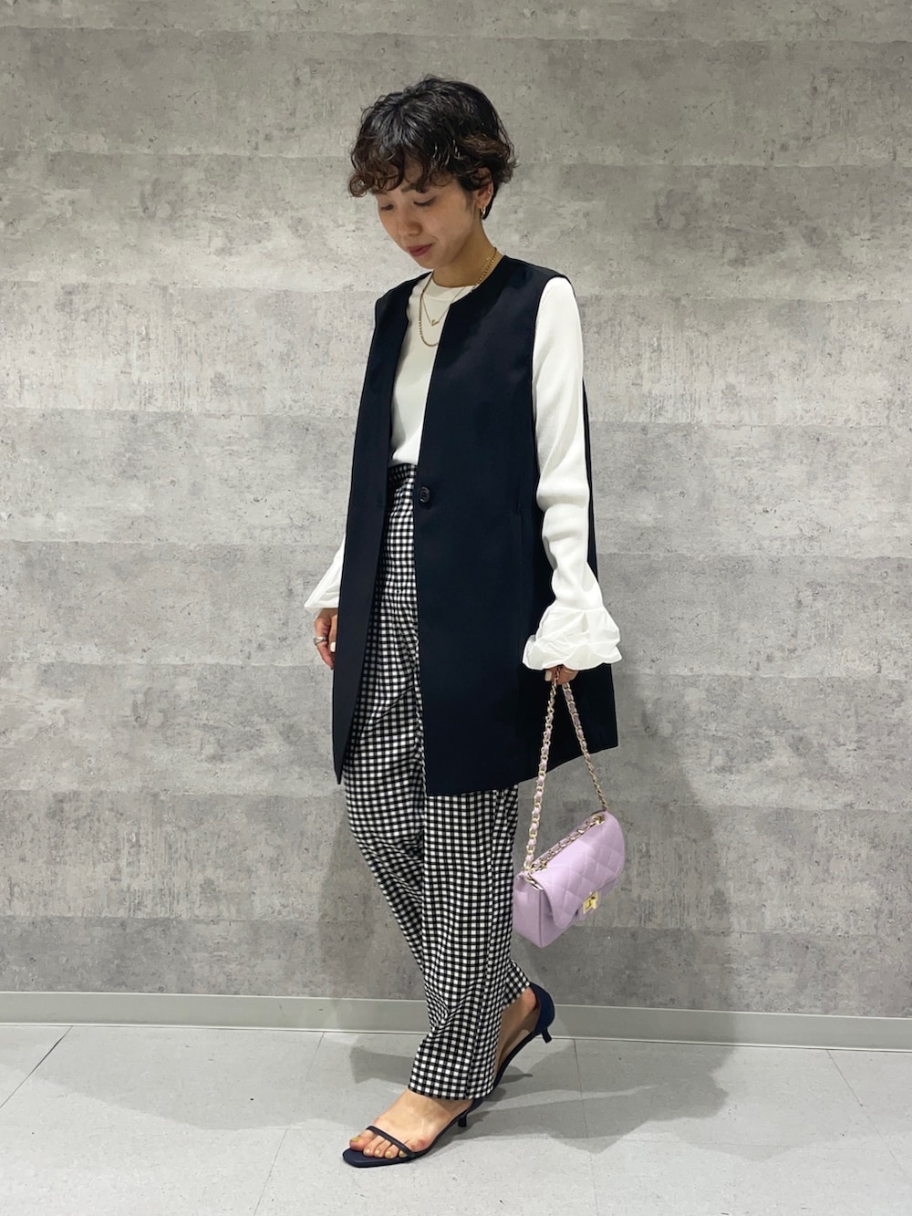 ブラック系のベスト、ホワイト系のニット/セーター、パープル系のショルダーバッグを着用したレディースの春コーディネートの3枚目の写真