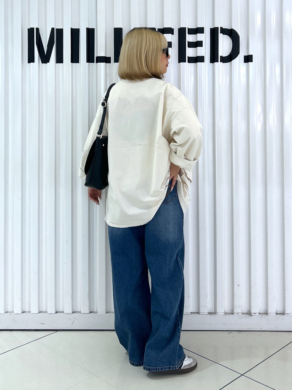 ホワイト系のミリタリージャケット、ブルー系のデニムパンツ、ブラック系のショルダーバッグを着用したレディースの秋コーディネートの3枚目の写真