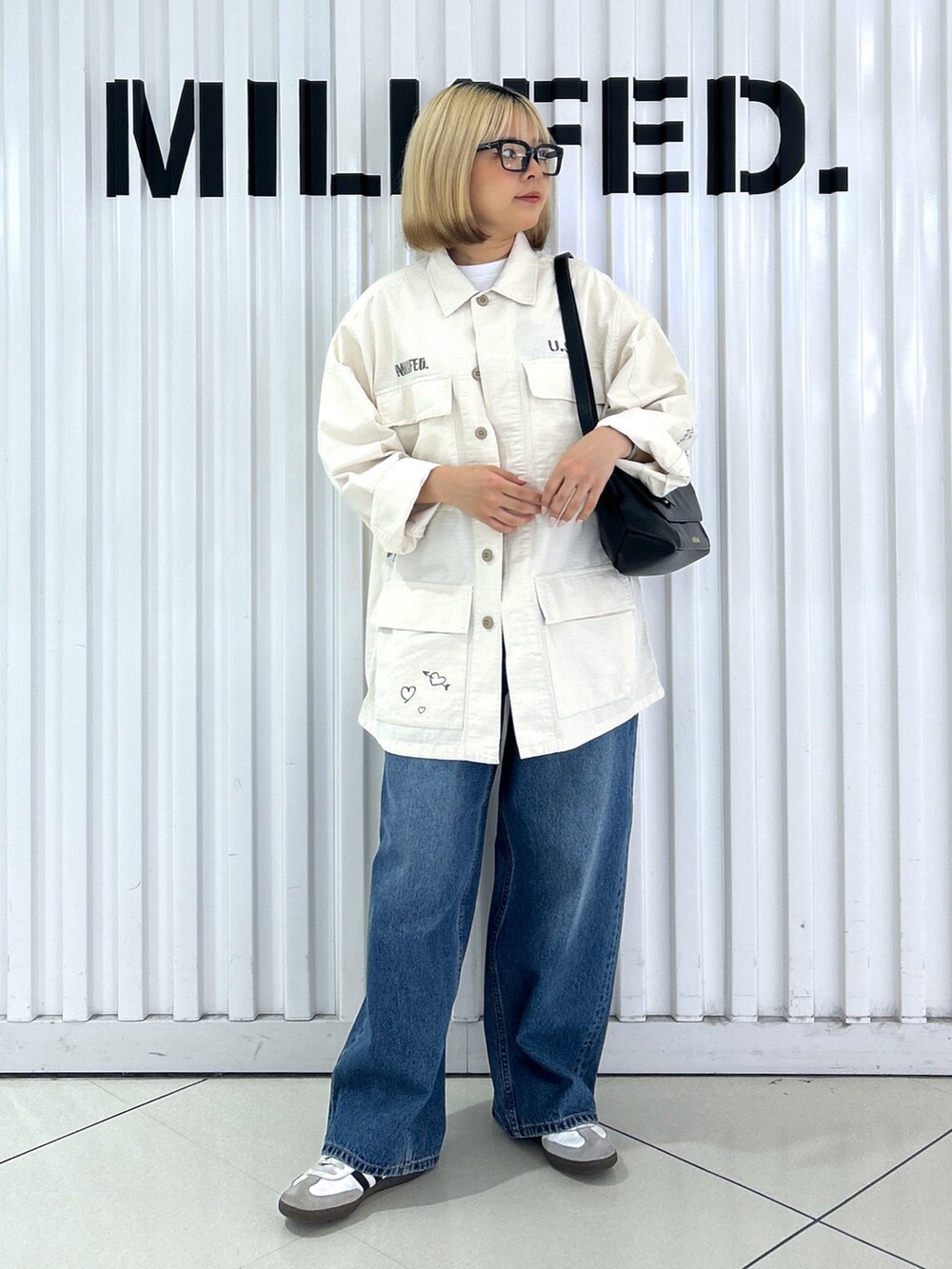 ホワイト系のミリタリージャケット、ブルー系のデニムパンツ、ブラック系のショルダーバッグを着用したレディースの秋コーディネートの2枚目の写真