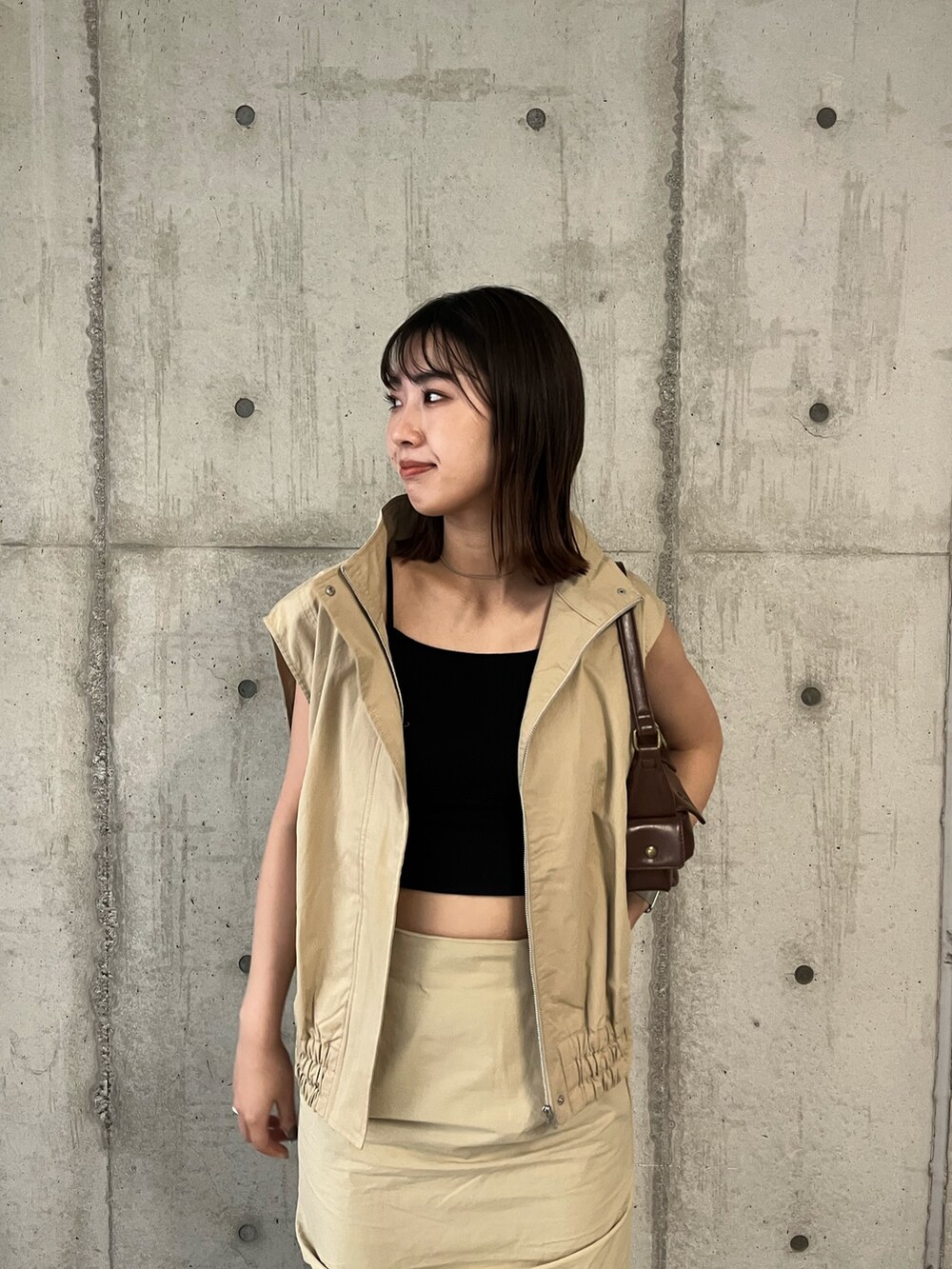 ベージュ系のベスト、ベージュ系のスカート、ブラウン系のハンドバッグを着用したレディースの夏コーディネートの5枚目の写真