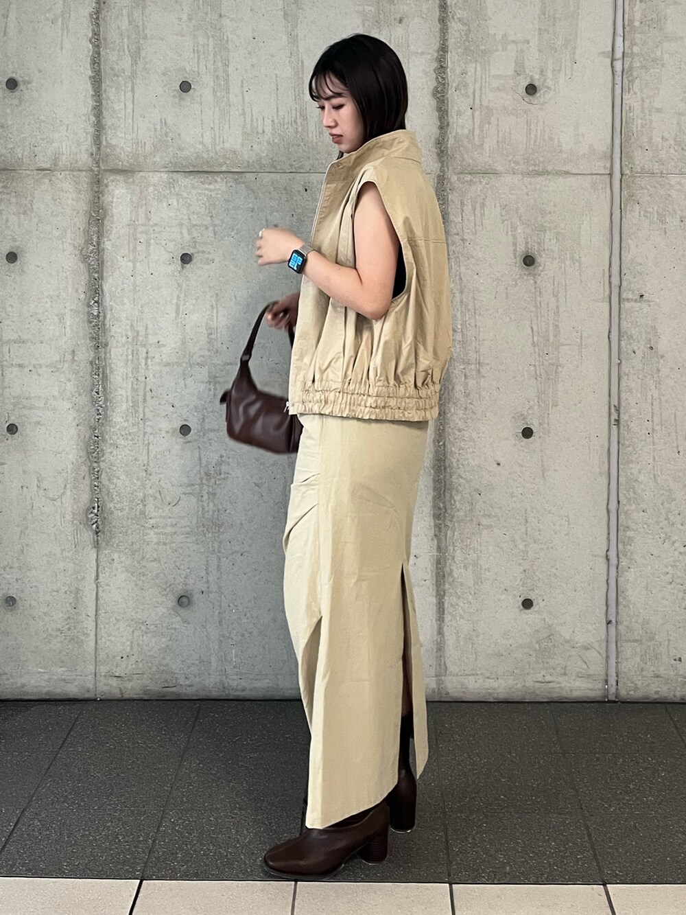ベージュ系のベスト、ベージュ系のスカート、ブラウン系のハンドバッグを着用したレディースの夏コーディネートの2枚目の写真