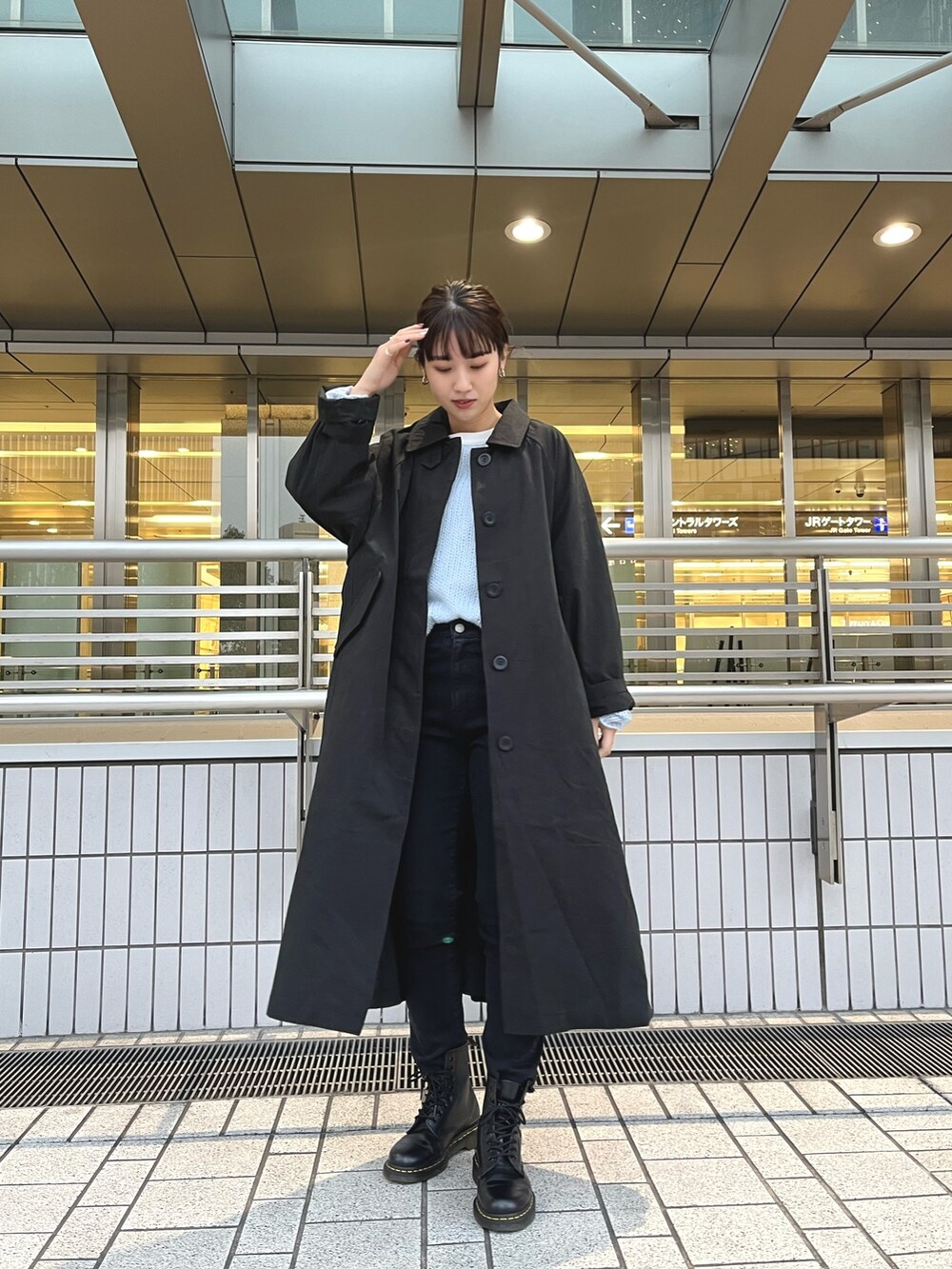 ブラック系のステンカラーコート、ブルー系のニット/セーター、ブラック系のデニムパンツを着用したレディースの冬コーディネートの2枚目の写真