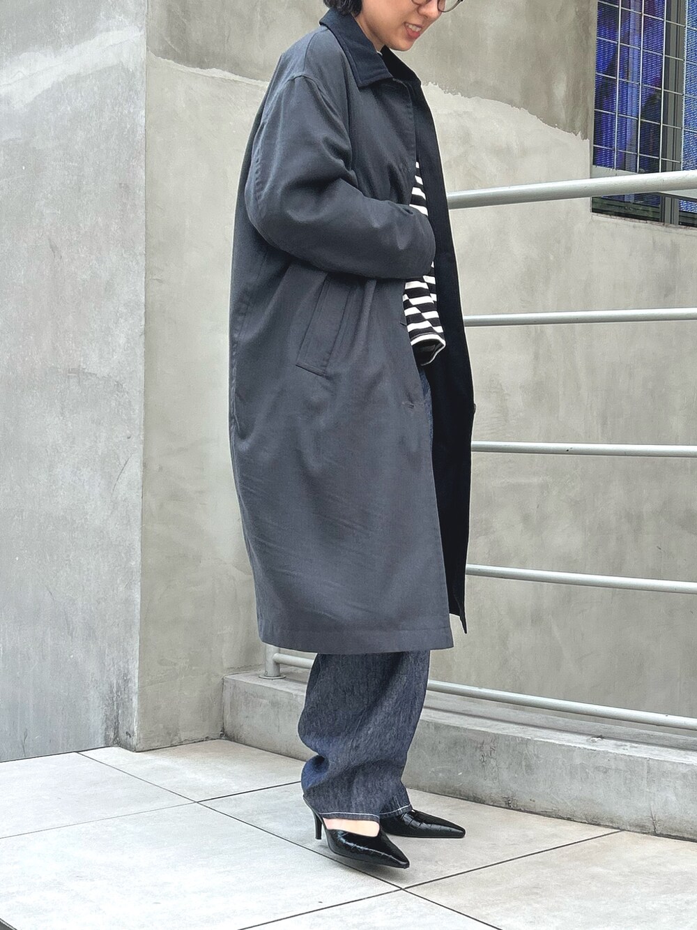 ブルー系のパンツ、グレー系のステンカラーコート、ブラック系のTシャツ/カットソーを着用したレディースの秋コーディネートの2枚目の写真