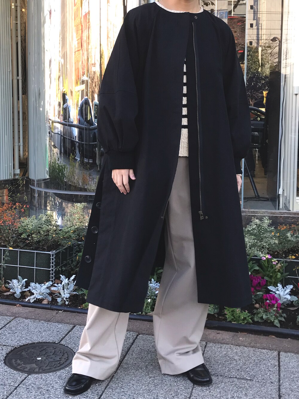 ブラック系のノーカラーコート、ベージュ系のスラックスを着用したレディースの冬コーディネートの3枚目の写真