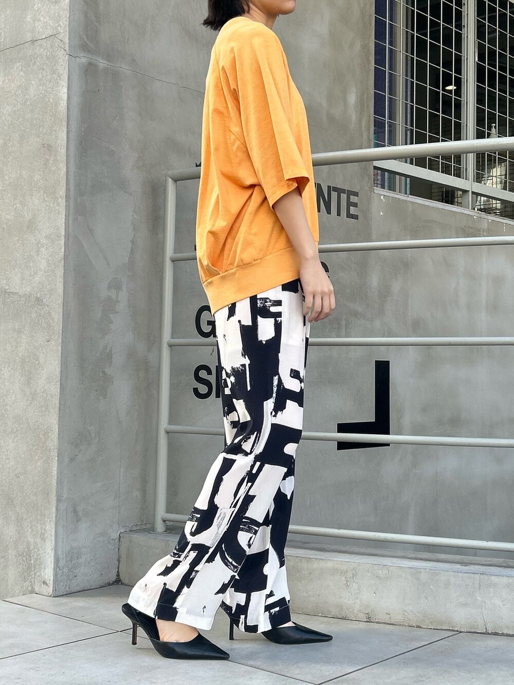 ブラック系のその他パンツ、オレンジ系のTシャツ/カットソーを着用したレディースの春コーディネートの2枚目の写真