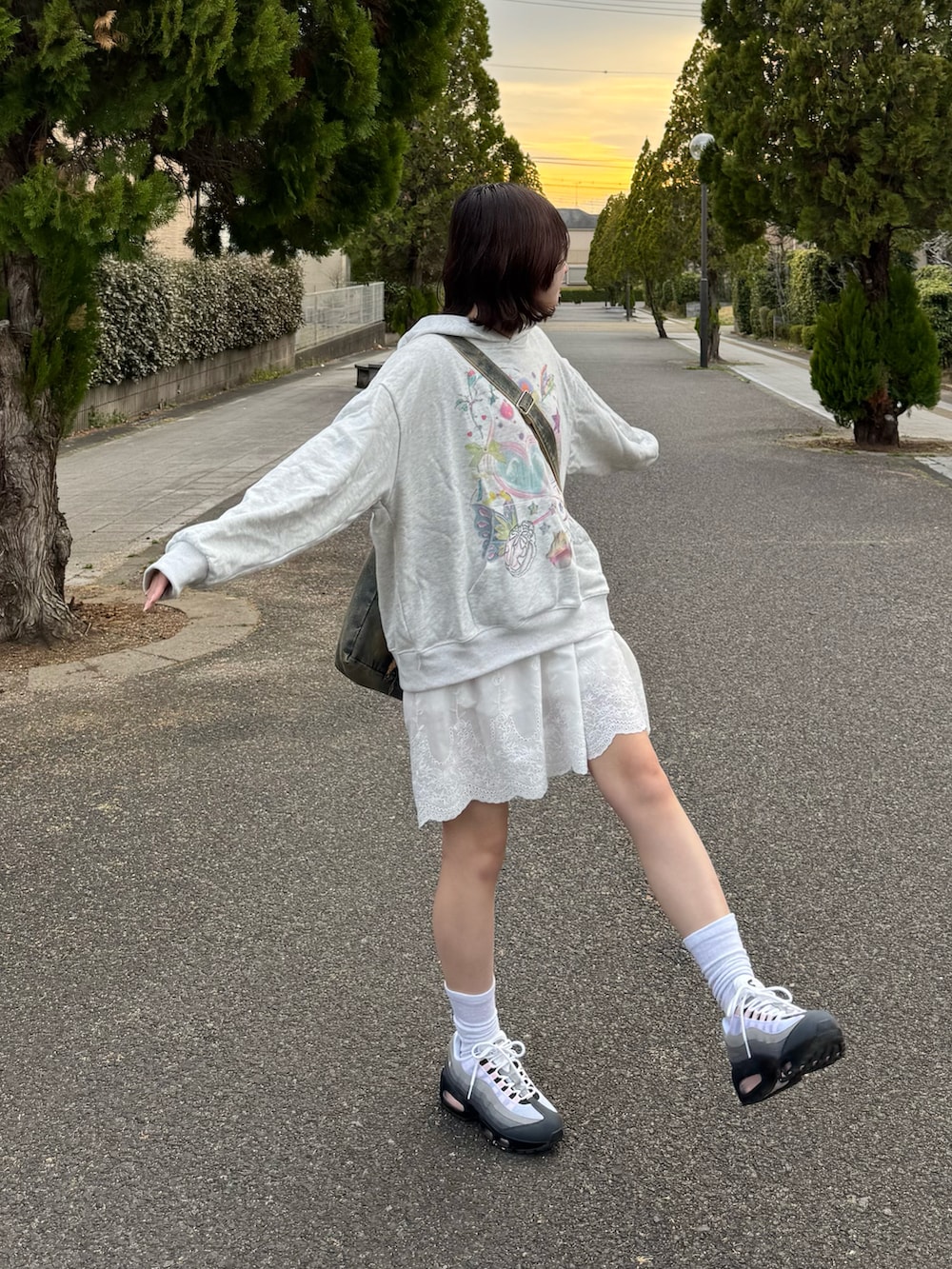 グレー系のパーカー、ホワイト系のワンピース、ブラック系のスニーカーを着用したレディースの春コーディネートの2枚目の写真