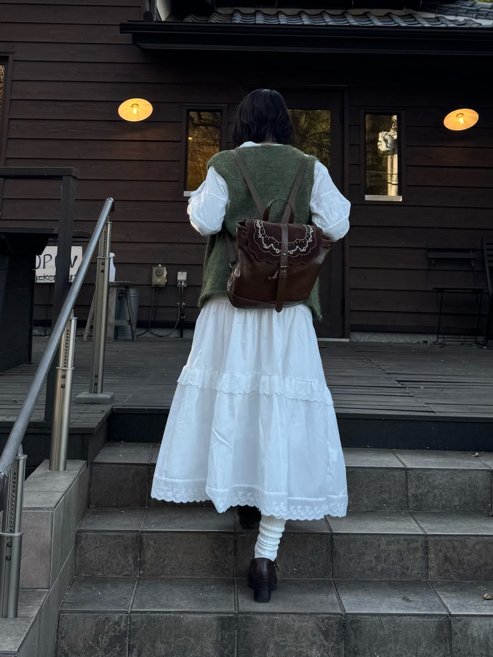 ホワイト系のスカート、ブラウン系のバックパック/リュック、グリーン系のベストを着用したレディースの冬コーディネートの3枚目の写真