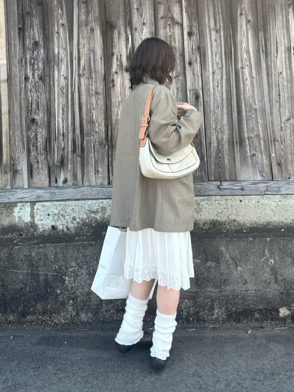 グレー系のテーラードジャケット、ブラウン系のスニーカー、ホワイト系のハンドバッグを着用したレディースの春コーディネートの2枚目の写真