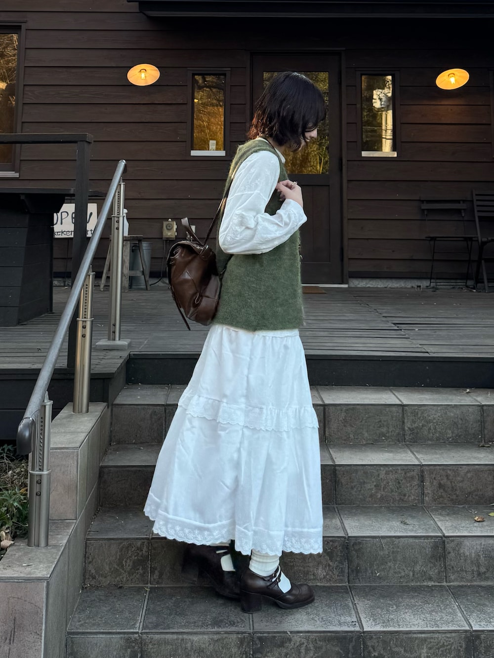 ホワイト系のスカート、ブラウン系のバックパック/リュック、グリーン系のベストを着用したレディースの冬コーディネートの2枚目の写真