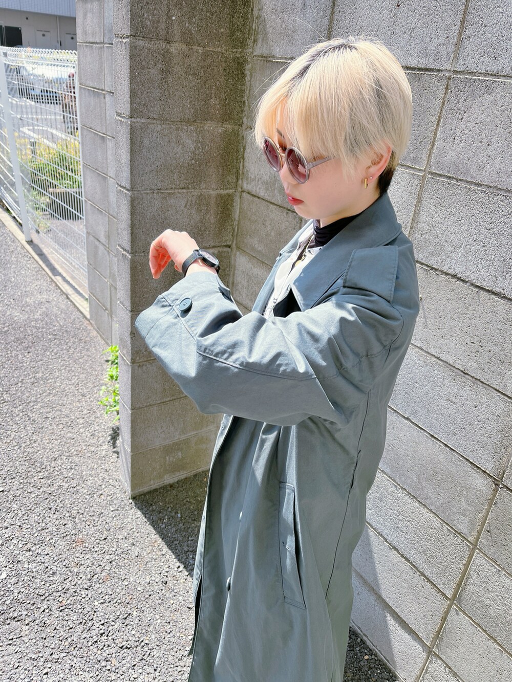 グリーン系のトレンチコート、ホワイト系のシャツ/ブラウス、ブラック系のサロペット/オーバーオールを着用したレディースの春コーディネートの3枚目の写真