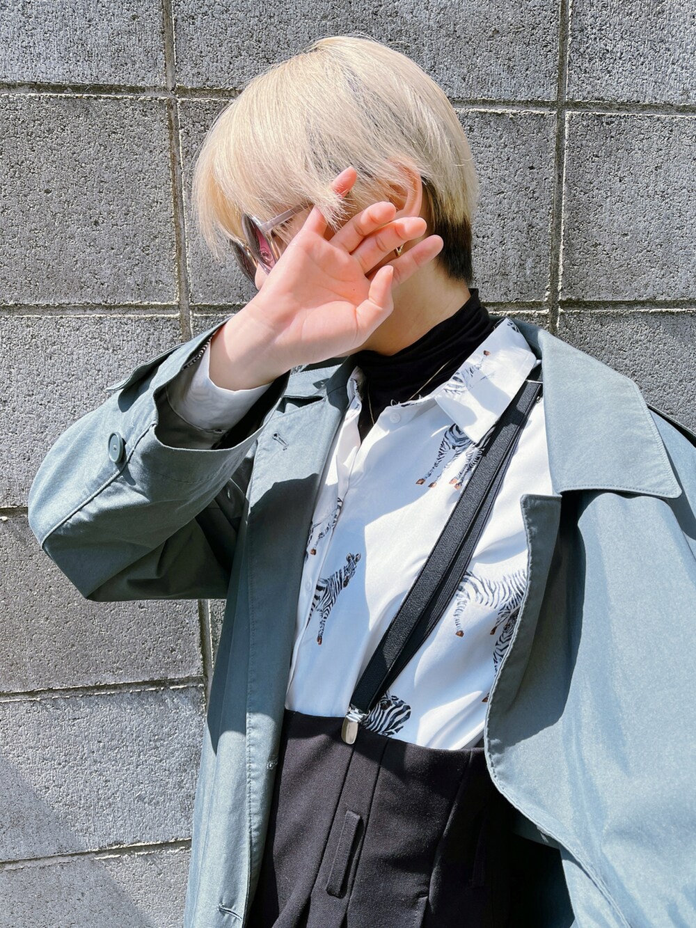 グリーン系のトレンチコート、ホワイト系のシャツ/ブラウス、ブラック系のサロペット/オーバーオールを着用したレディースの春コーディネートの2枚目の写真