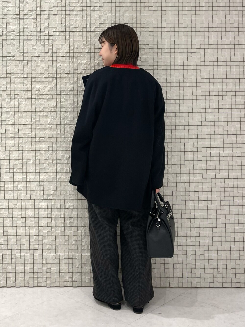 レッド系のニット/セーター、ブラック系のノーカラーコート、グレー系のその他パンツを着用したレディースの冬コーディネートの3枚目の写真