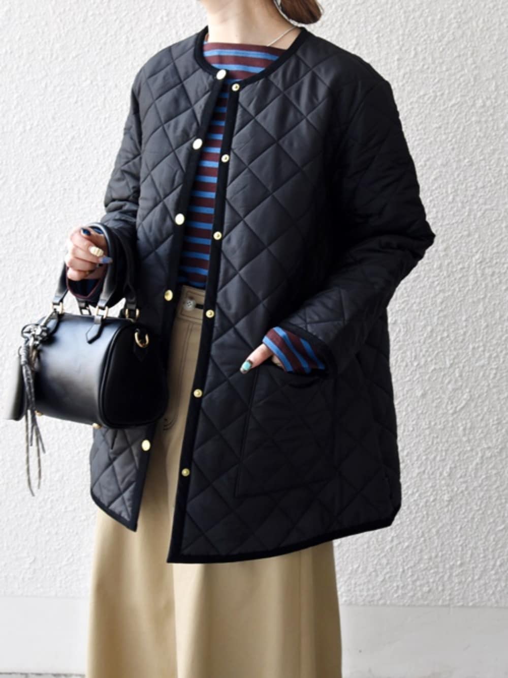 ベージュ系のスカート、ブラック系のノーカラーコートを着用したレディースの秋コーディネートの4枚目の写真