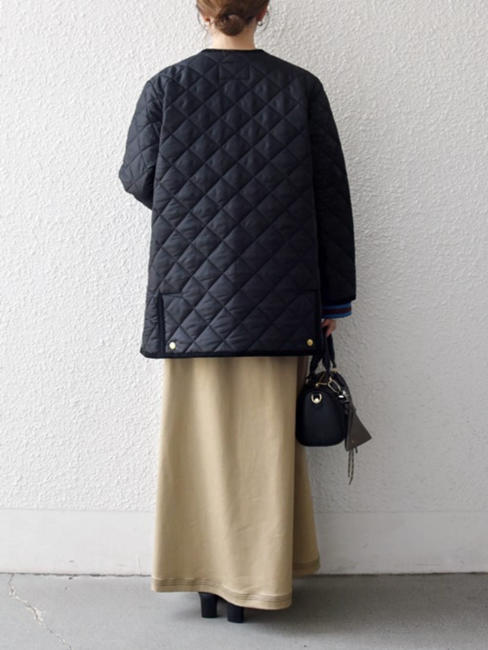 ベージュ系のスカート、ブラック系のノーカラーコートを着用したレディースの秋コーディネートの2枚目の写真