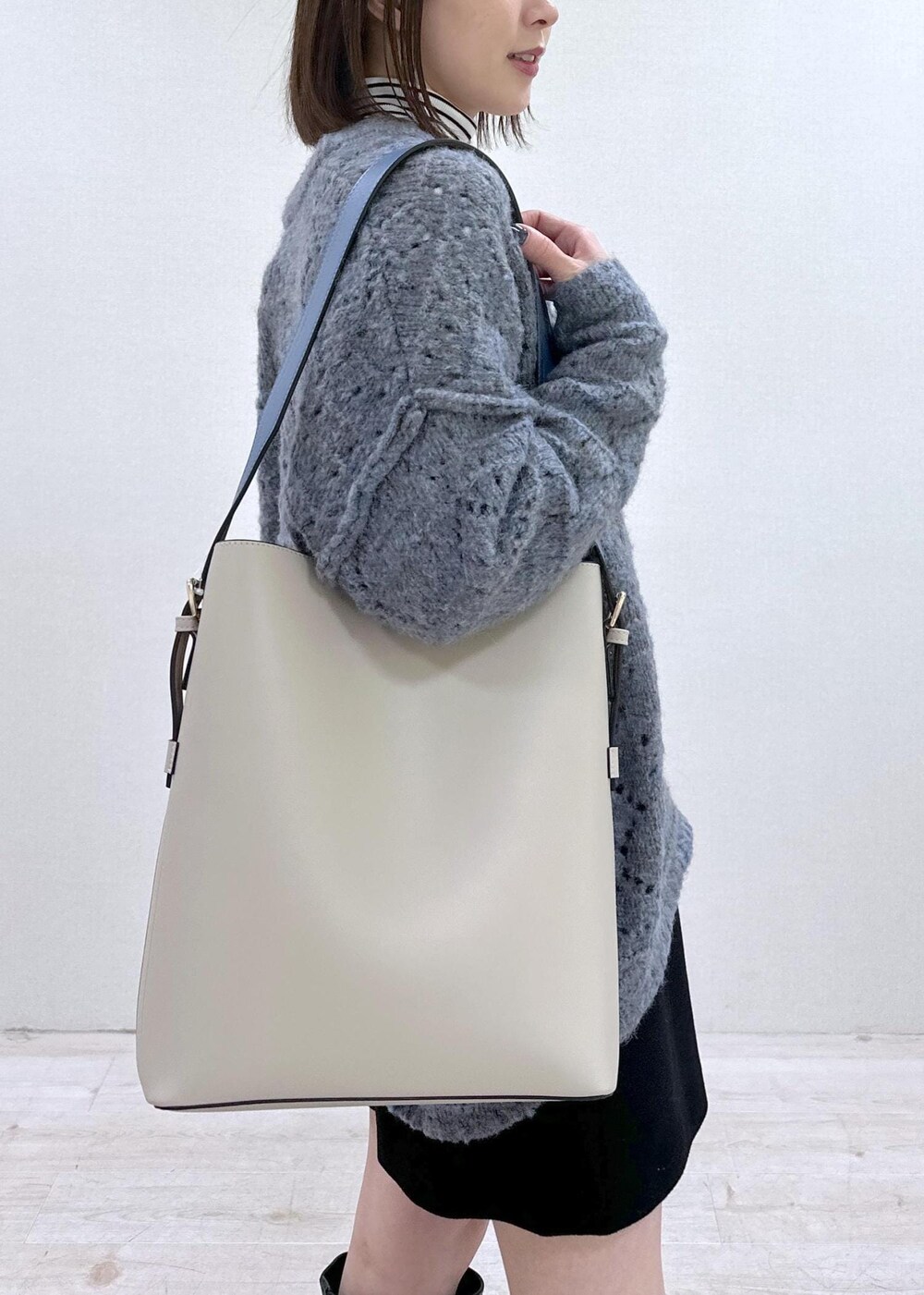 ベージュ系のショルダーバッグ、ブルー系のニット/セーター、ホワイト系のTシャツ/カットソーを着用したレディースの冬コーディネートの6枚目の写真