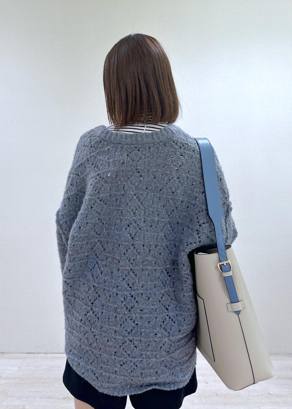 ベージュ系のショルダーバッグ、ブルー系のニット/セーター、ホワイト系のTシャツ/カットソーを着用したレディースの冬コーディネートの7枚目の写真