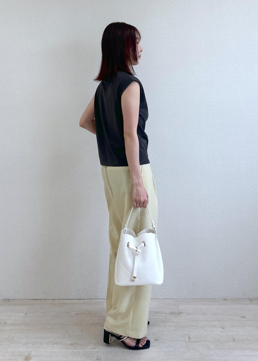 ホワイト系のショルダーバッグ、ブラック系のサンダル、イエロー系のスラックスを着用したレディースの夏コーディネートの2枚目の写真