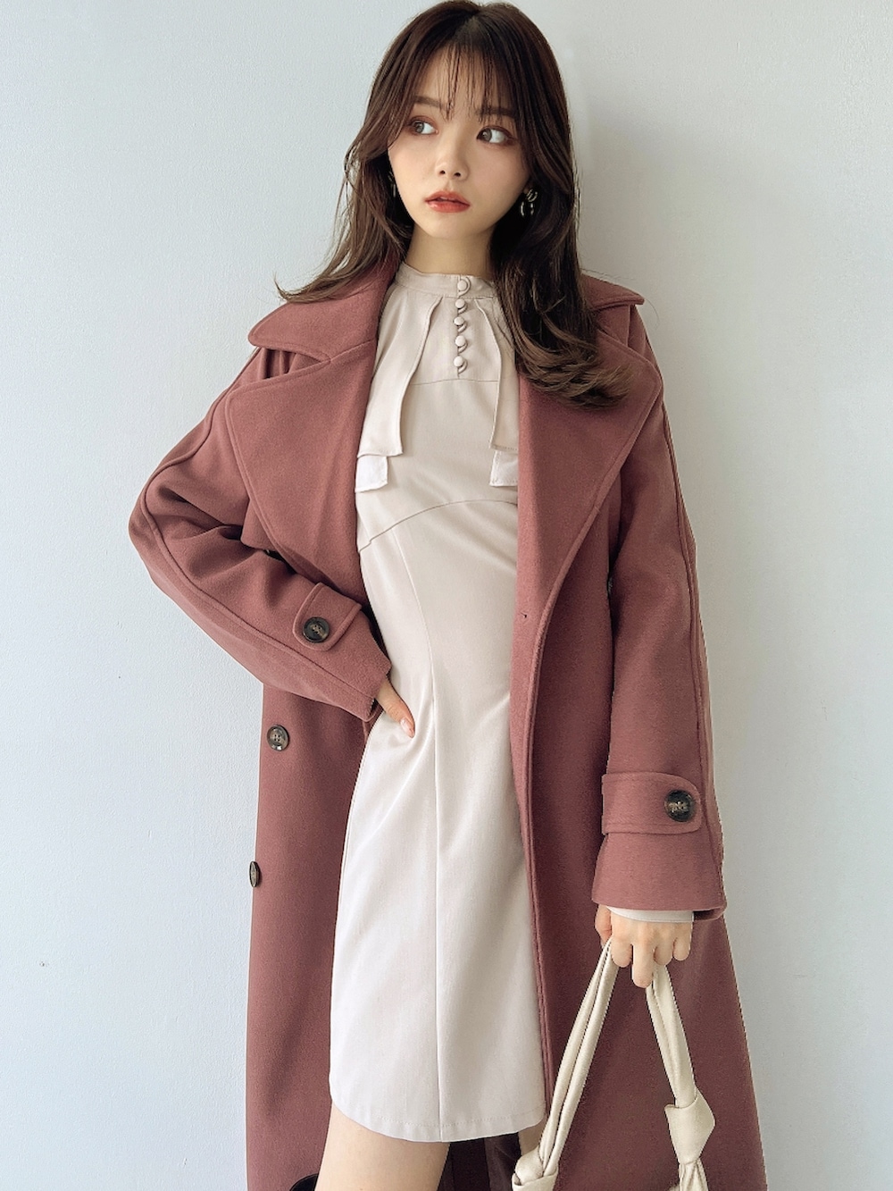 ピンク系のトレンチコート、ホワイト系のワンピース、ホワイト系のハンドバッグを着用したレディースの冬コーディネートの3枚目の写真