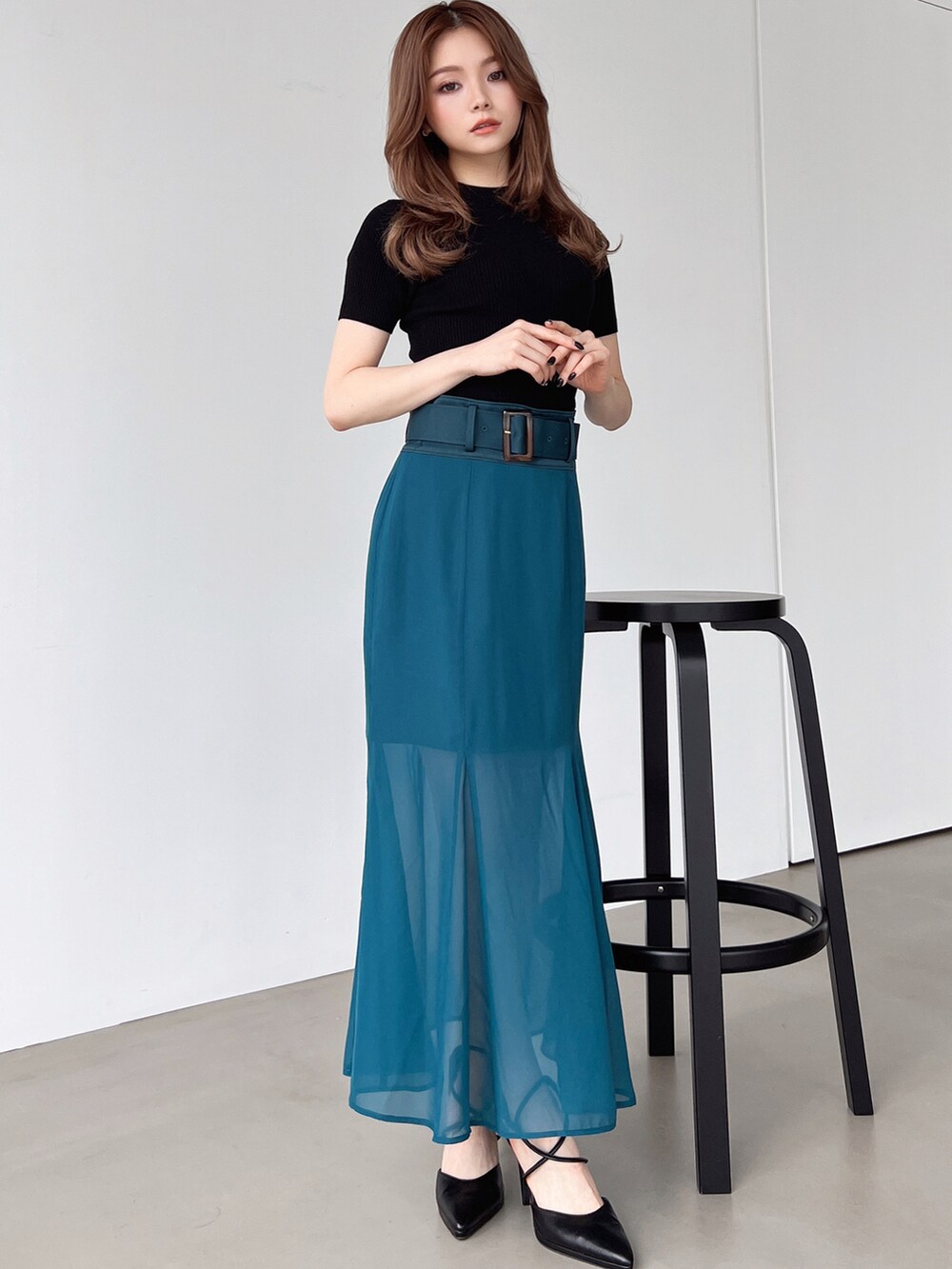 グリーン系のスカート、ブラック系のパンプス、ブラック系のニット/セーターを着用したレディースの夏コーディネートの2枚目の写真