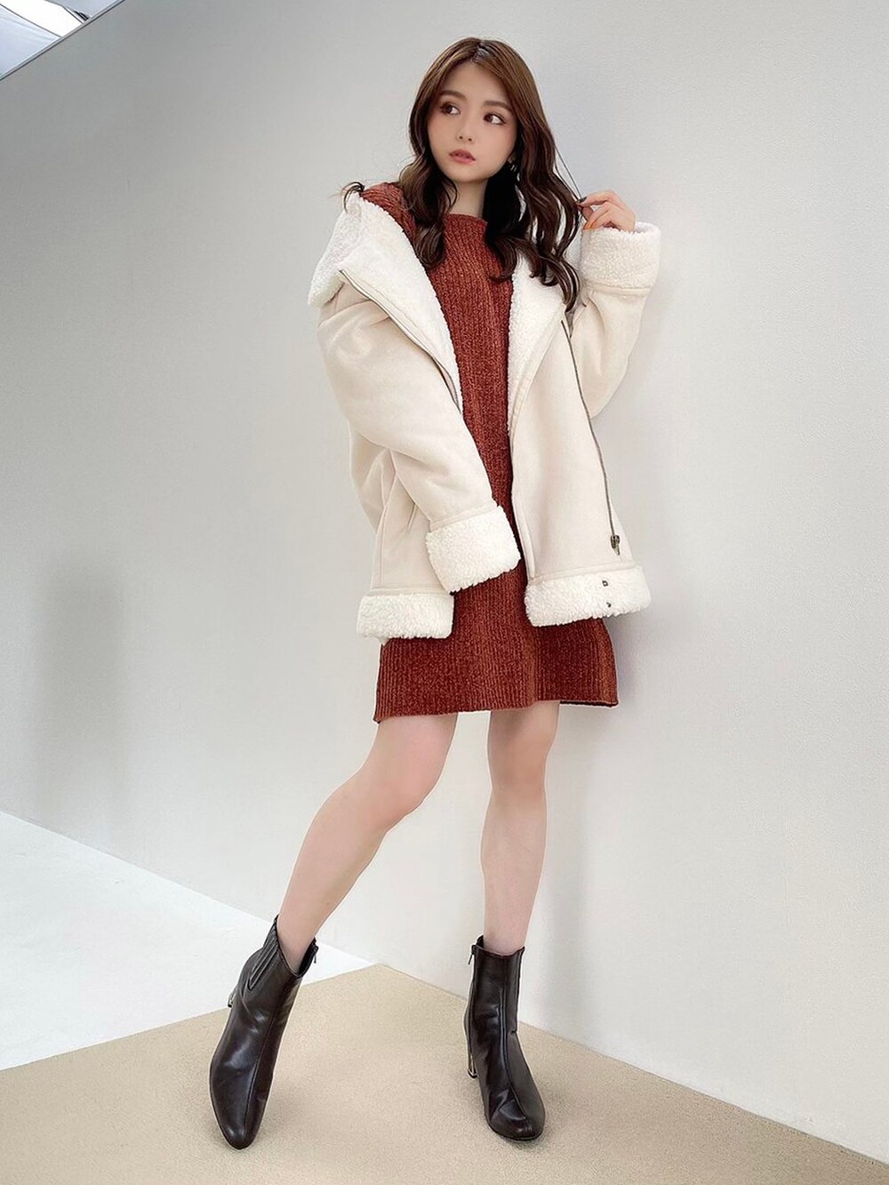 ホワイト系のムートンコート、ブラウン系のブーツ、オレンジ系のワンピースを着用したレディースの秋コーディネートの2枚目の写真