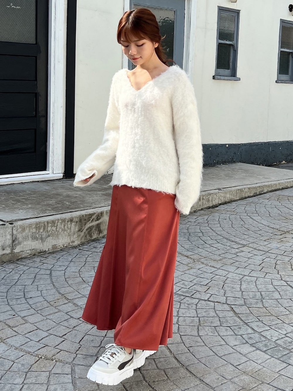 グレー系のスニーカー、ホワイト系のニット/セーター、オレンジ系のスカートを着用したレディースの冬コーディネートの2枚目の写真