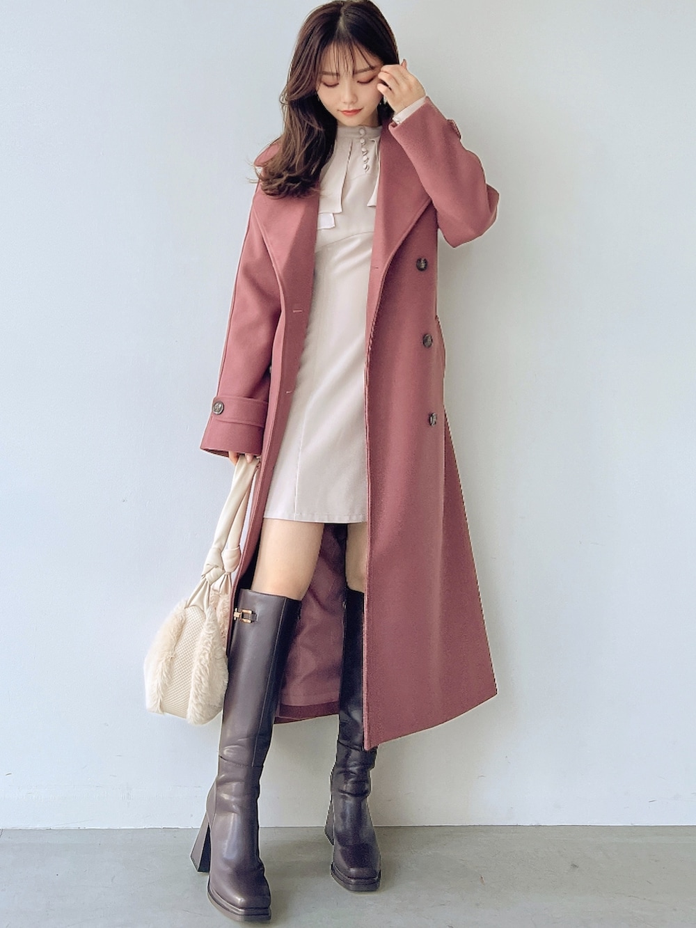 ピンク系のトレンチコート、ホワイト系のワンピース、ホワイト系のハンドバッグを着用したレディースの冬コーディネートの2枚目の写真