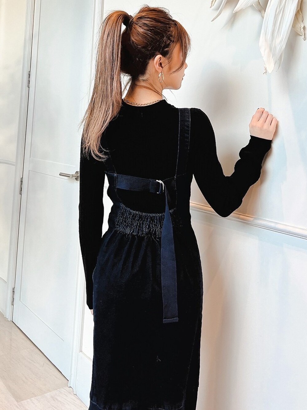 ブラック系のニット/セーター、ブルー系のジャンパースカート、ベージュ系のサンダルを着用したレディースの冬コーディネートの2枚目の写真