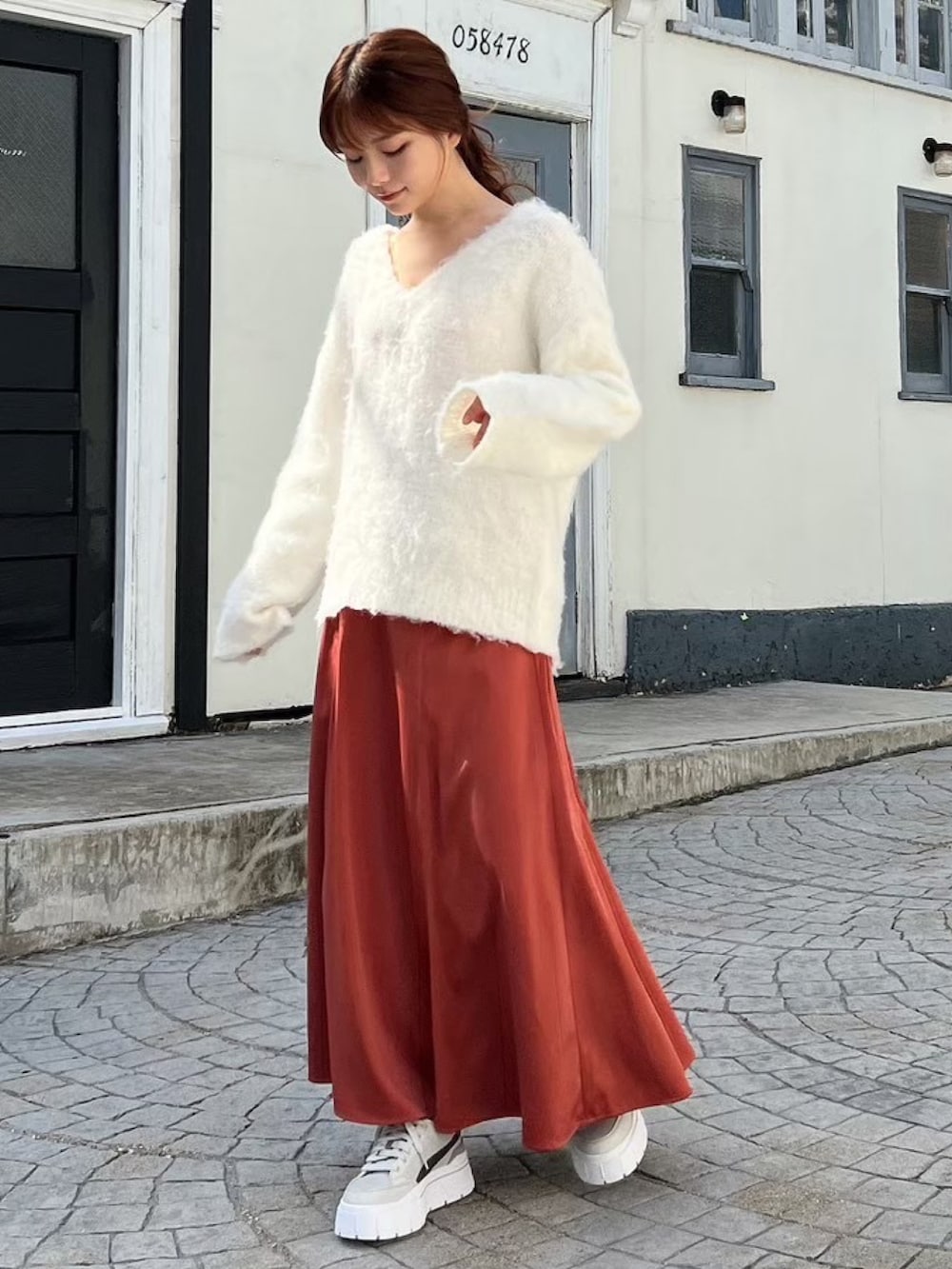 グレー系のスニーカー、ホワイト系のニット/セーター、オレンジ系のスカートを着用したレディースの冬コーディネートの3枚目の写真