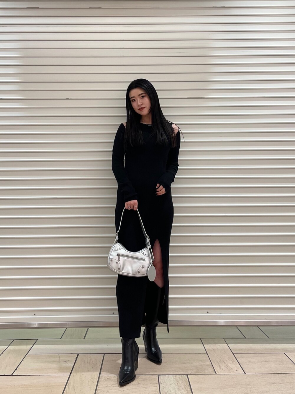 ブラック系のワンピース、シルバー系のハンドバッグ、ブラック系のブーツを着用したレディースの春コーディネートの2枚目の写真