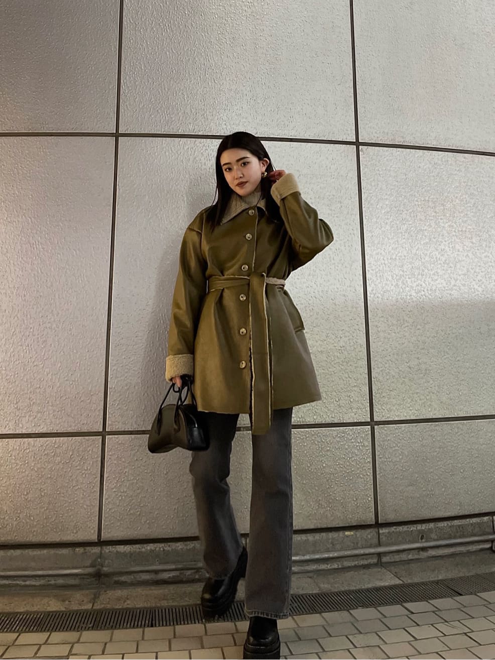 ブラック系のハンドバッグ、ベージュ系のムートンコート、ホワイト系のニット/セーターを着用したレディースの冬コーディネートの2枚目の写真