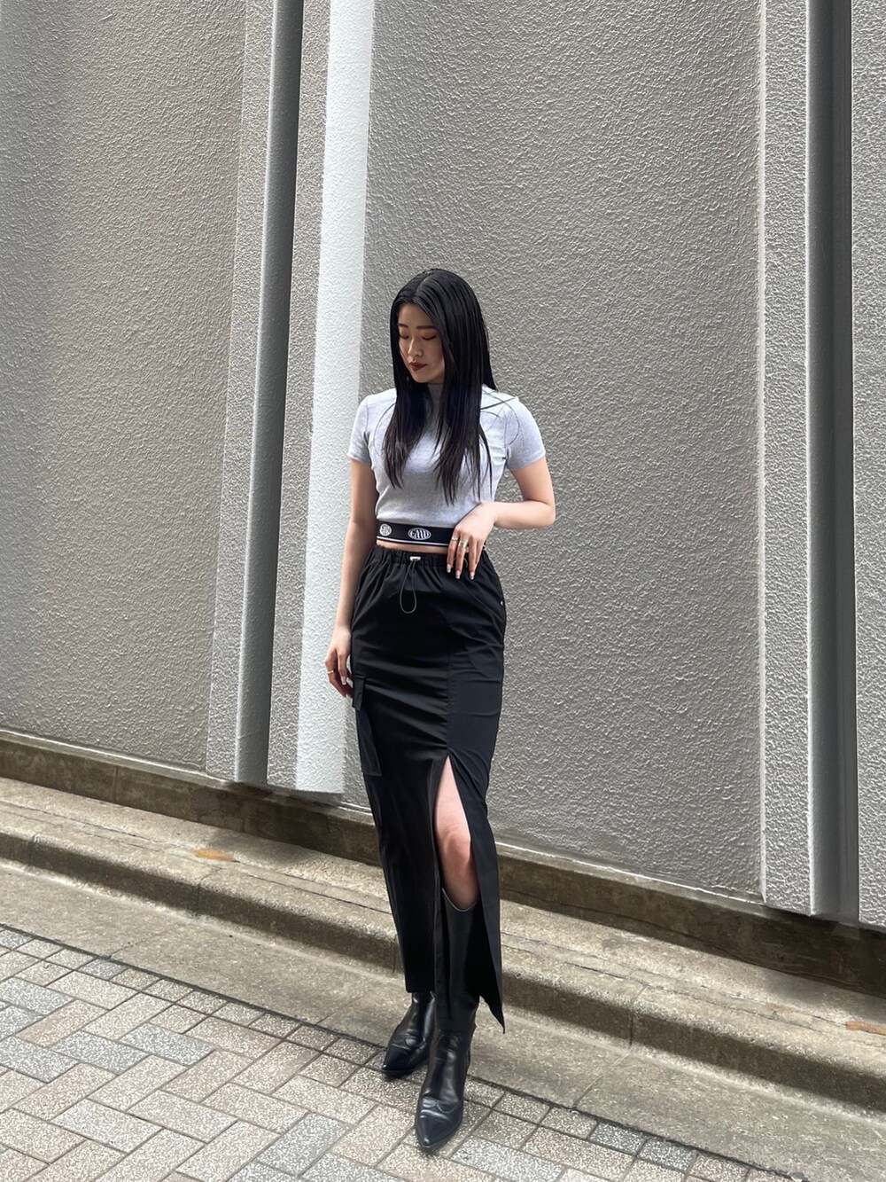 ブラック系のスカート、グレー系のTシャツ/カットソー、ブラック系のブーツを着用したレディースの春コーディネートの2枚目の写真