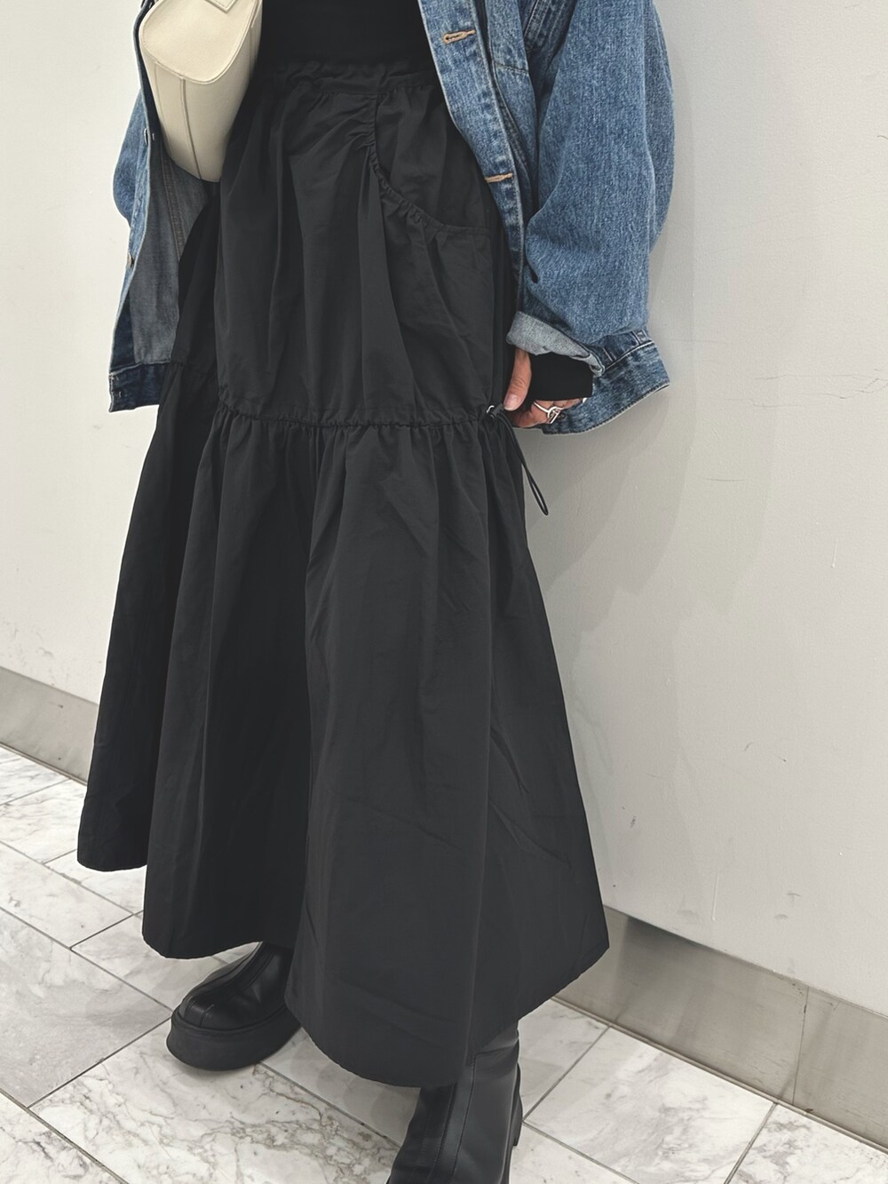 ブルー系のデニムジャケット、ブラック系のワンピース、ホワイト系のショルダーバッグを着用したレディースの秋コーディネートの4枚目の写真