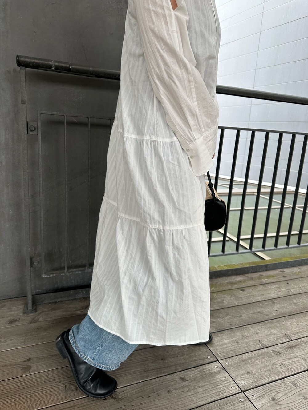 ホワイト系のワンピース、ブルー系のデニムパンツ、ブラック系のハンドバッグを着用したレディースの春コーディネートの3枚目の写真