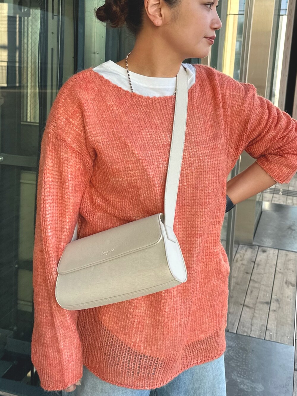 オレンジ系のニット/セーター、ホワイト系のショルダーバッグ、ブルー系のデニムパンツを着用したレディースの秋コーディネートの3枚目の写真