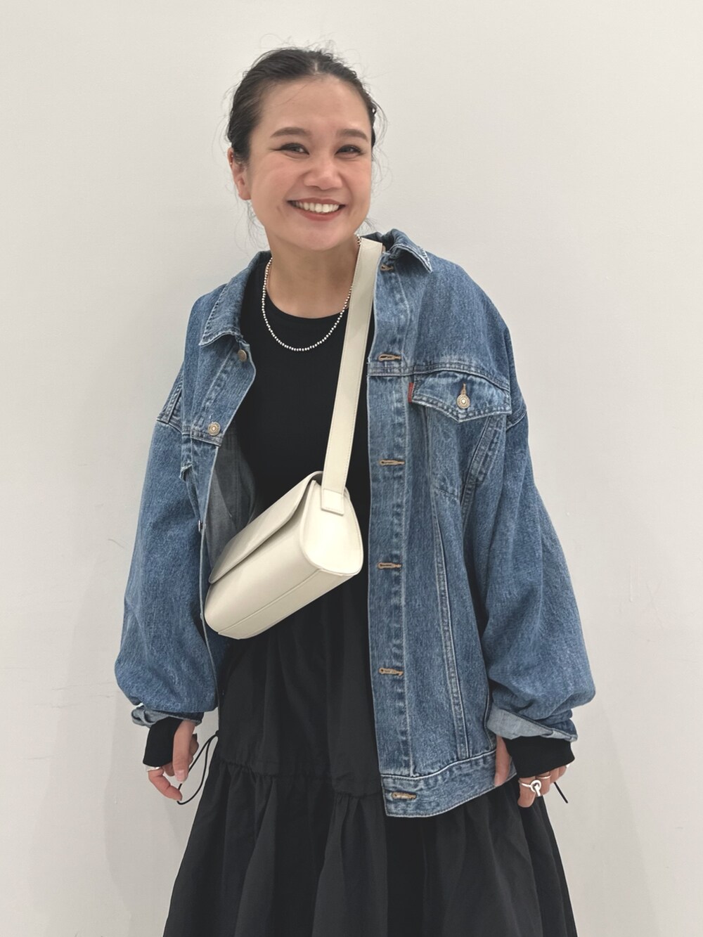 ブルー系のデニムジャケット、ブラック系のワンピース、ホワイト系のショルダーバッグを着用したレディースの秋コーディネートの3枚目の写真