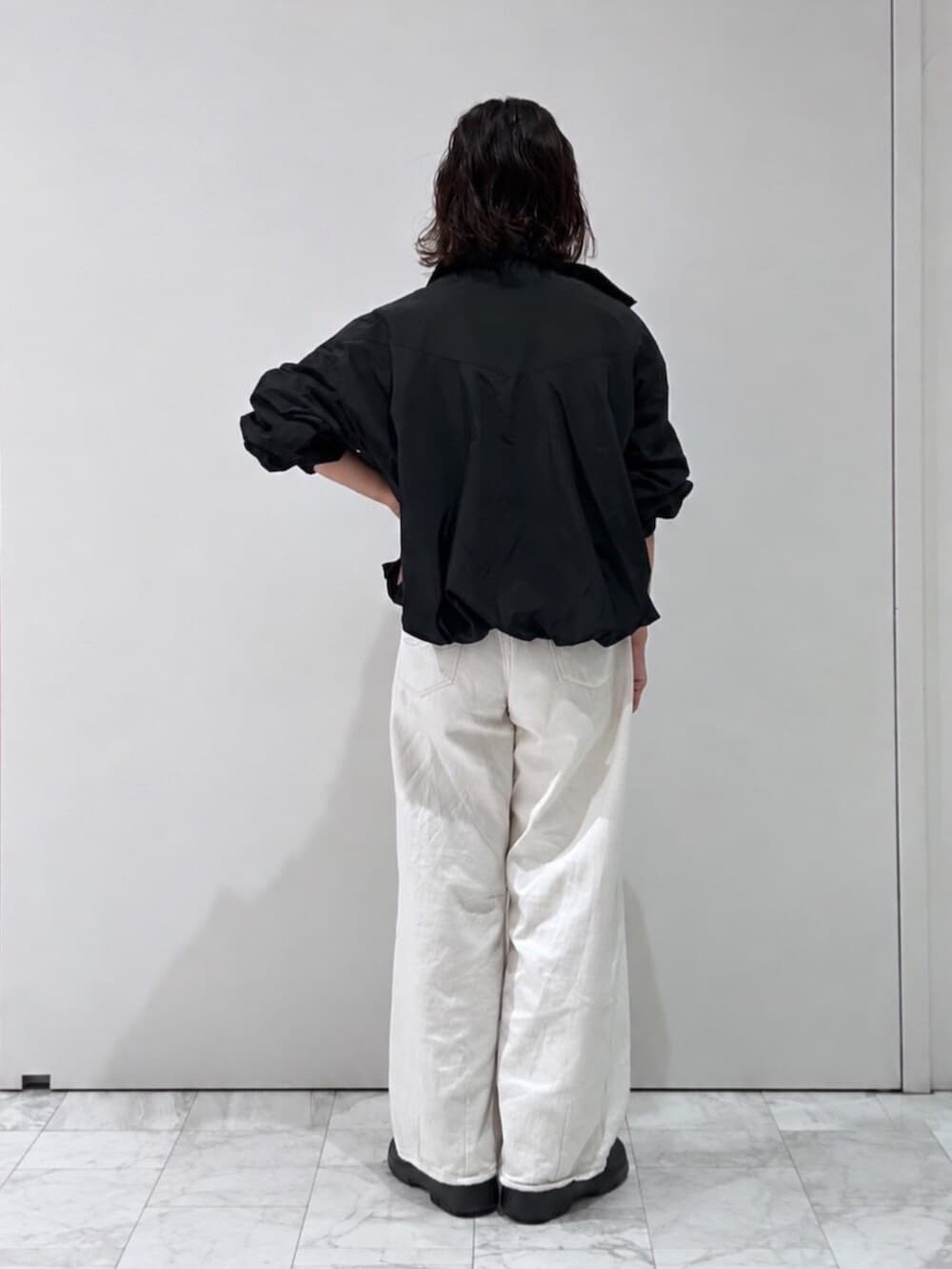 ブラック系のブルゾン、ホワイト系のニット/セーター、ホワイト系のデニムパンツを着用したレディースの夏コーディネートの3枚目の写真