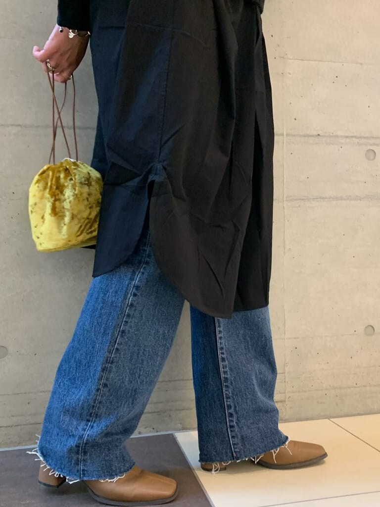 ブルー系のデニムパンツ、ブラック系のワンピース、イエロー系のハンドバッグを着用したレディースの秋コーディネートの3枚目の写真