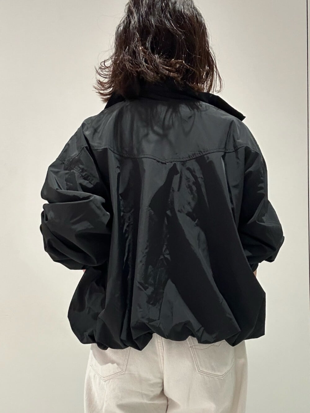 ブラック系のブルゾン、ホワイト系のニット/セーター、ホワイト系のデニムパンツを着用したレディースの夏コーディネートの5枚目の写真