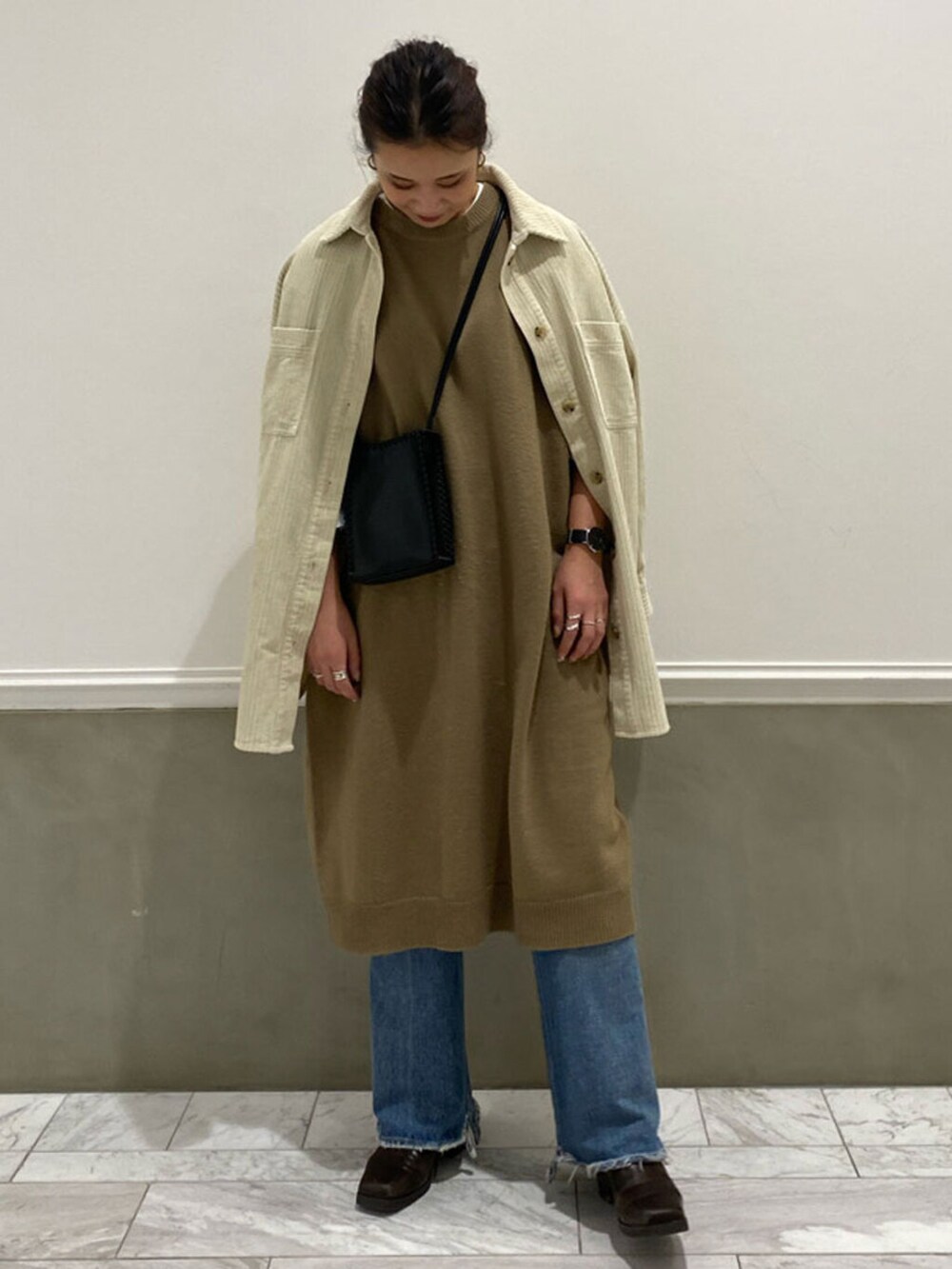 グレー系のワンピース、ブルー系のデニムパンツ、ブラウン系のブーツを着用したレディースの秋コーディネートの2枚目の写真