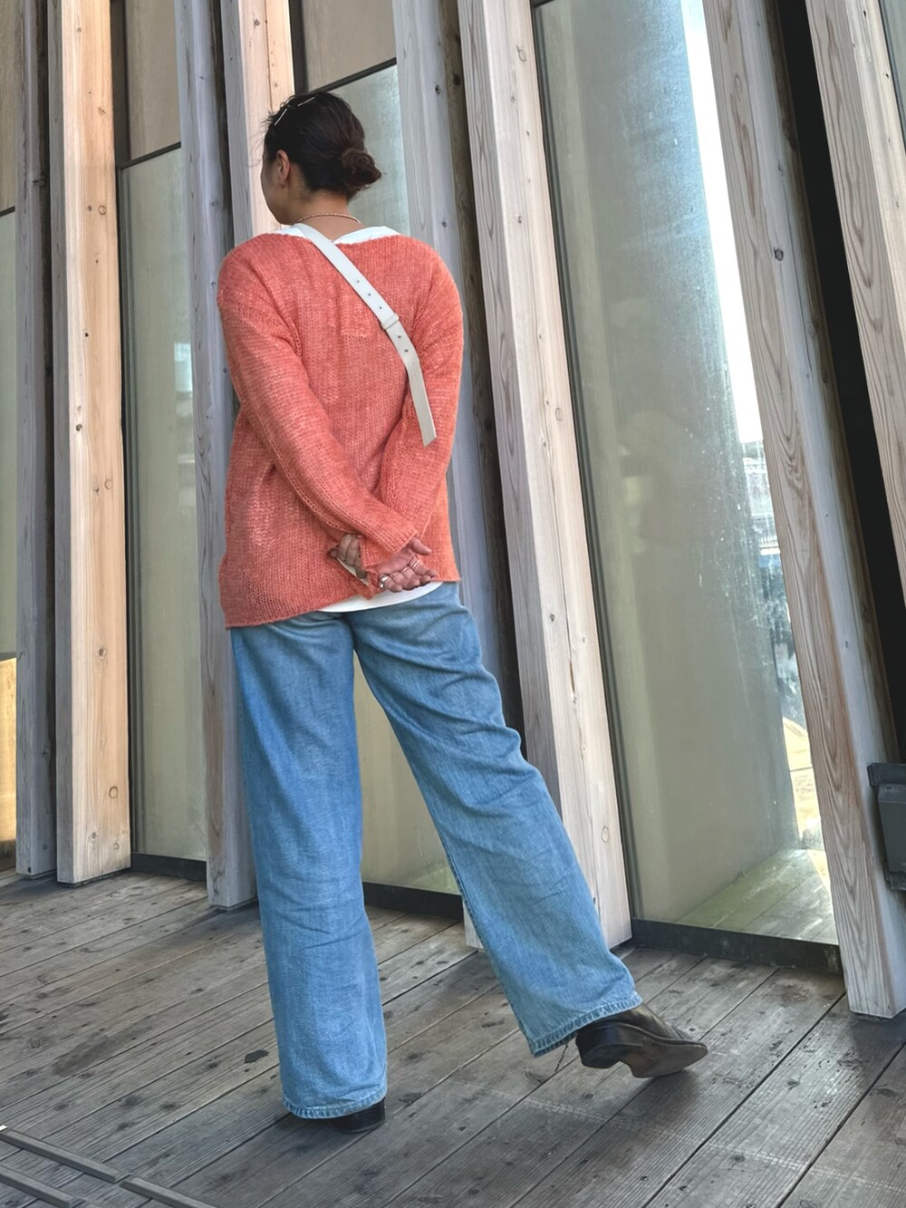 オレンジ系のニット/セーター、ホワイト系のショルダーバッグ、ブルー系のデニムパンツを着用したレディースの秋コーディネートの2枚目の写真