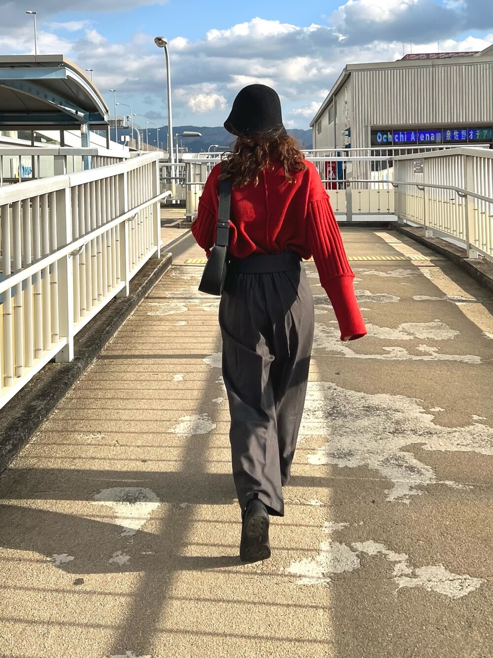 レッド系のニット/セーター、グレー系のスラックスを着用したレディースの秋コーディネートの2枚目の写真