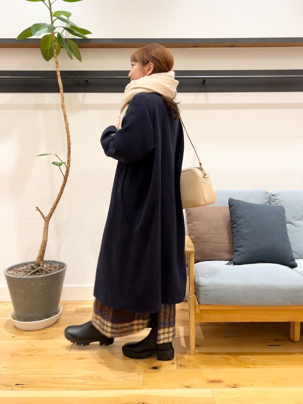 グレー系のステンカラーコート、ブラウン系のスカート、ブラック系のブーツを着用したレディースの冬コーディネートの3枚目の写真