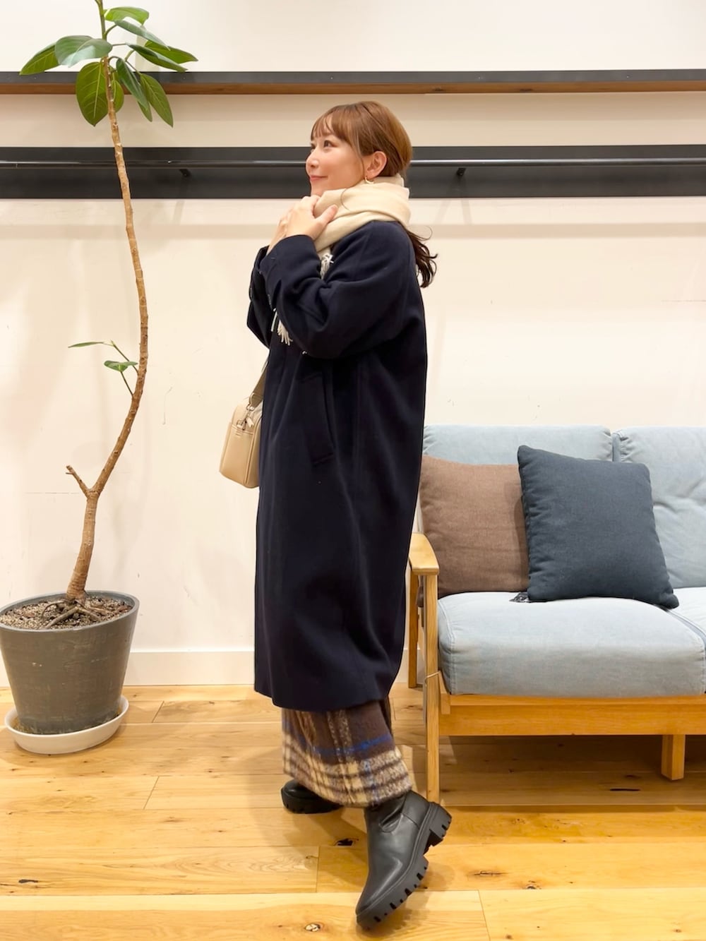 グレー系のステンカラーコート、ブラウン系のスカート、ブラック系のブーツを着用したレディースの冬コーディネートの2枚目の写真