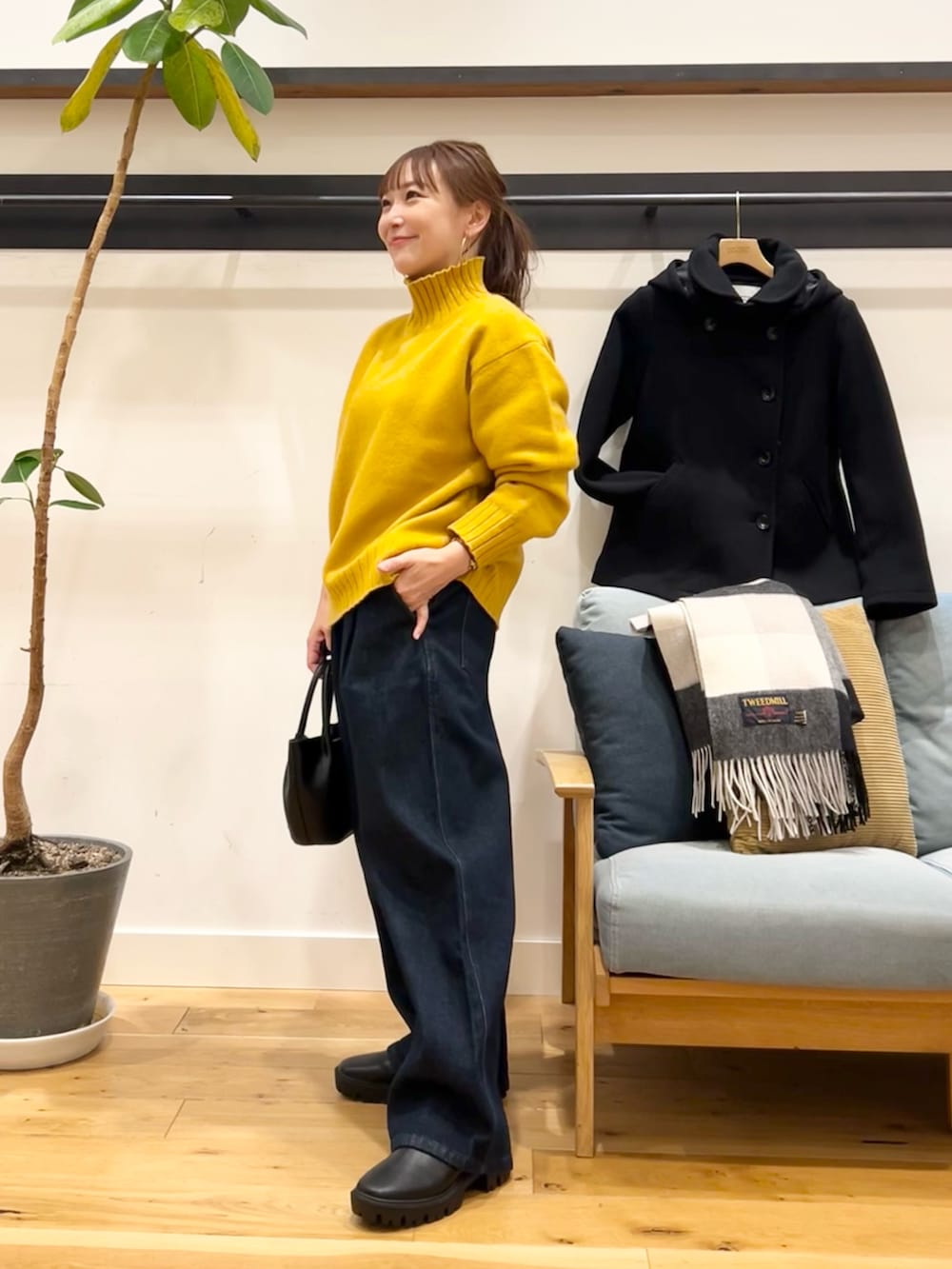 イエロー系のニット/セーター、ブルー系のデニムパンツ、ブラック系のショルダーバッグを着用したレディースの冬コーディネートの2枚目の写真
