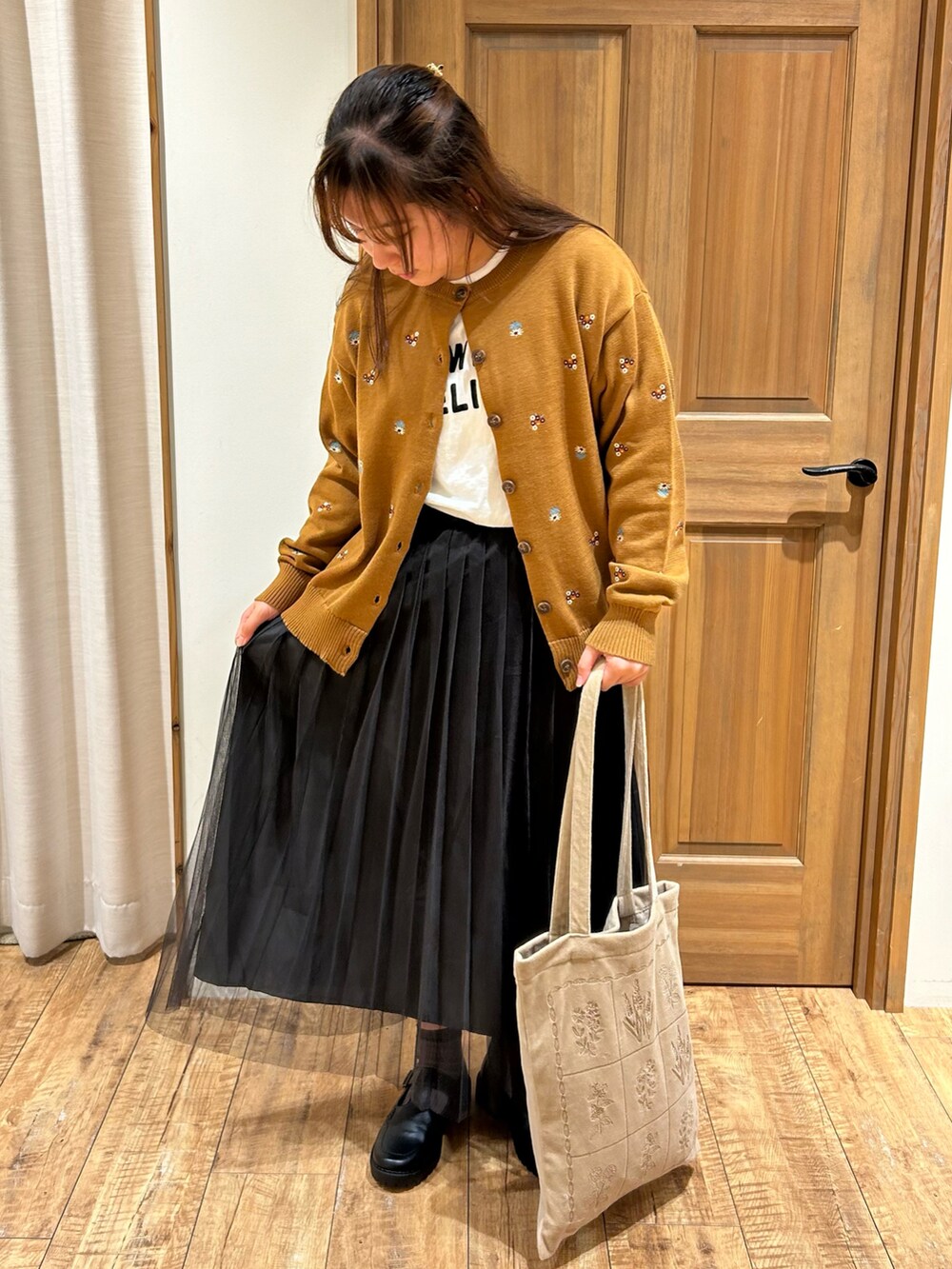 イエロー系のカーディガン/ボレロ、ホワイト系のTシャツ/カットソー、グレー系のスカートを着用したレディースの秋コーディネートの2枚目の写真